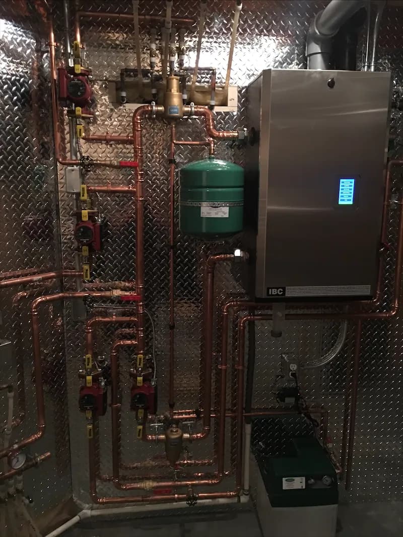Stainless condensing boiler with a green expansion tank, copper manifold and floor-mounted circulator in a basement mechanical room
