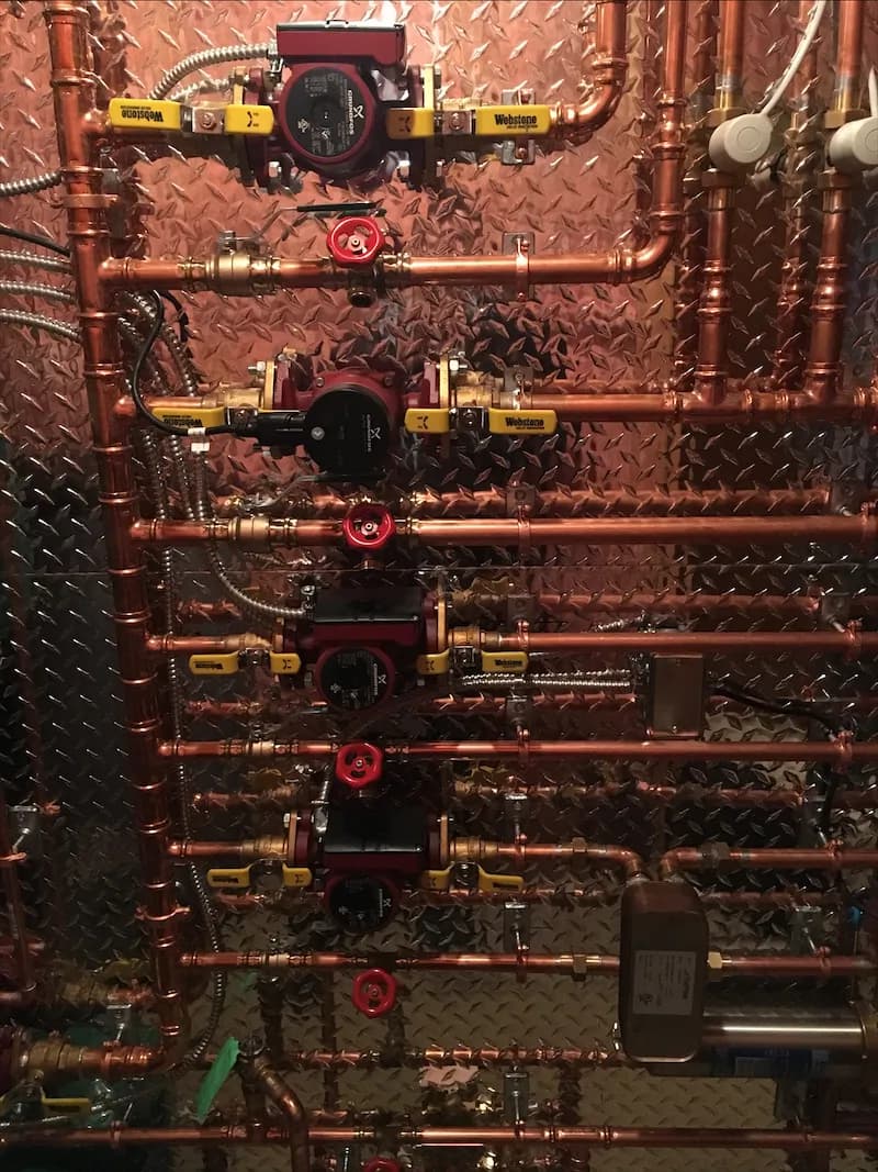 Copper manifold with brass unions and red-handled zone valves feeding separate heating zones