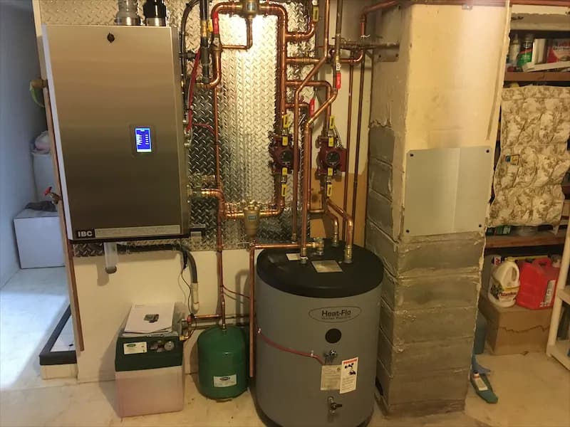 A pair of wall-mounted boilers piped in copper beside an insulated hot water tank