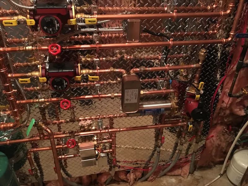 Close view of a copper hydronic manifold with brass fittings and red-handled zone valves